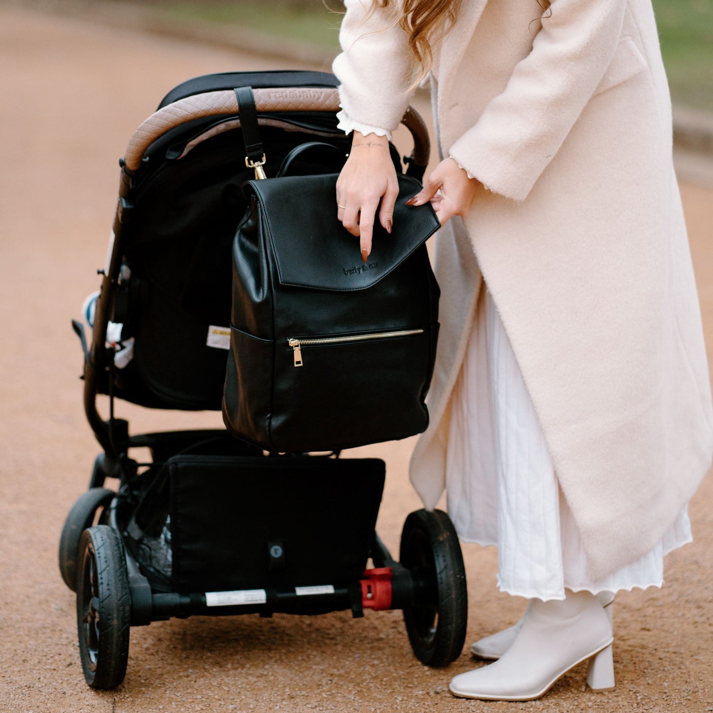 Parent hanging Florence black nappy bag on stroller with pram straps while out with baby