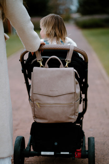 Parent and toddler in the park with Florence taupe nappy bag hanging off stroller with pram straps